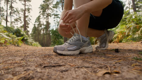 Primer-Plano-De-Una-Mujer-Atándose-Los-Cordones-De-Una-Zapatilla-Deportiva-Antes-De-Hacer-Ejercicio-Corriendo-Por-Una-Pista-A-Través-Del-Bosque,-Filmado-En-Tiempo-Real-2